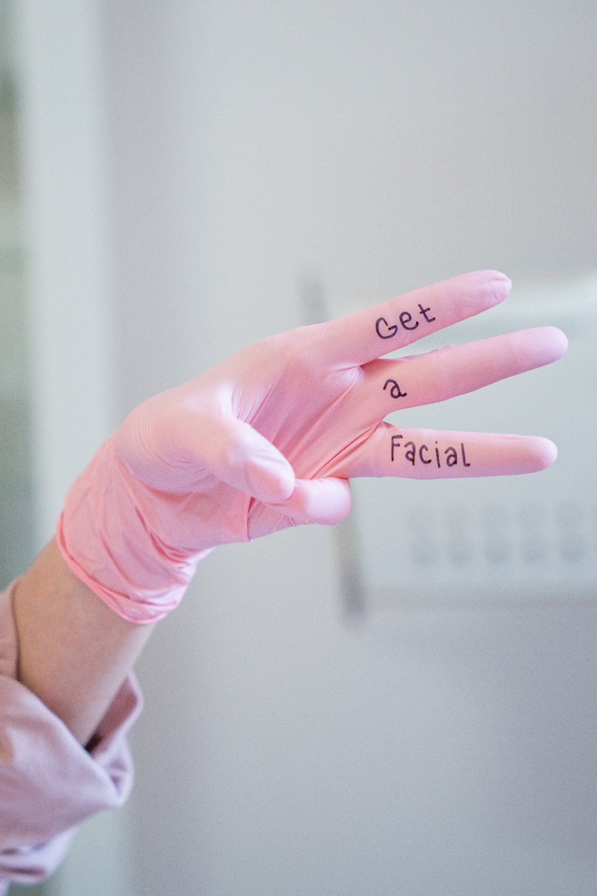 Ruka v růžové rukavici s nápisem Get a Facial — hravý detail ze salonu