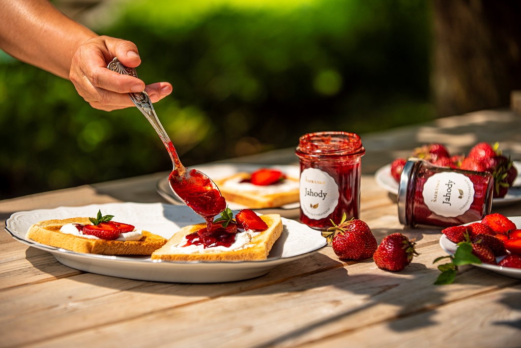 Ruka nabírá jahodovou marmeládu Šafránka lžičkou na toast s tvarohem — lifestyle záběr